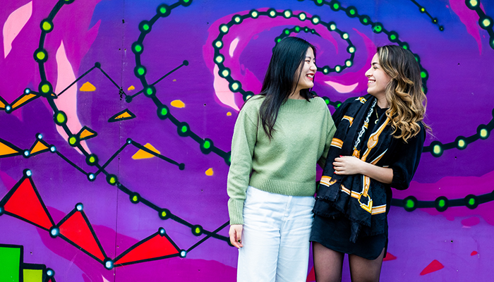 Two women standing in front pf purple wall